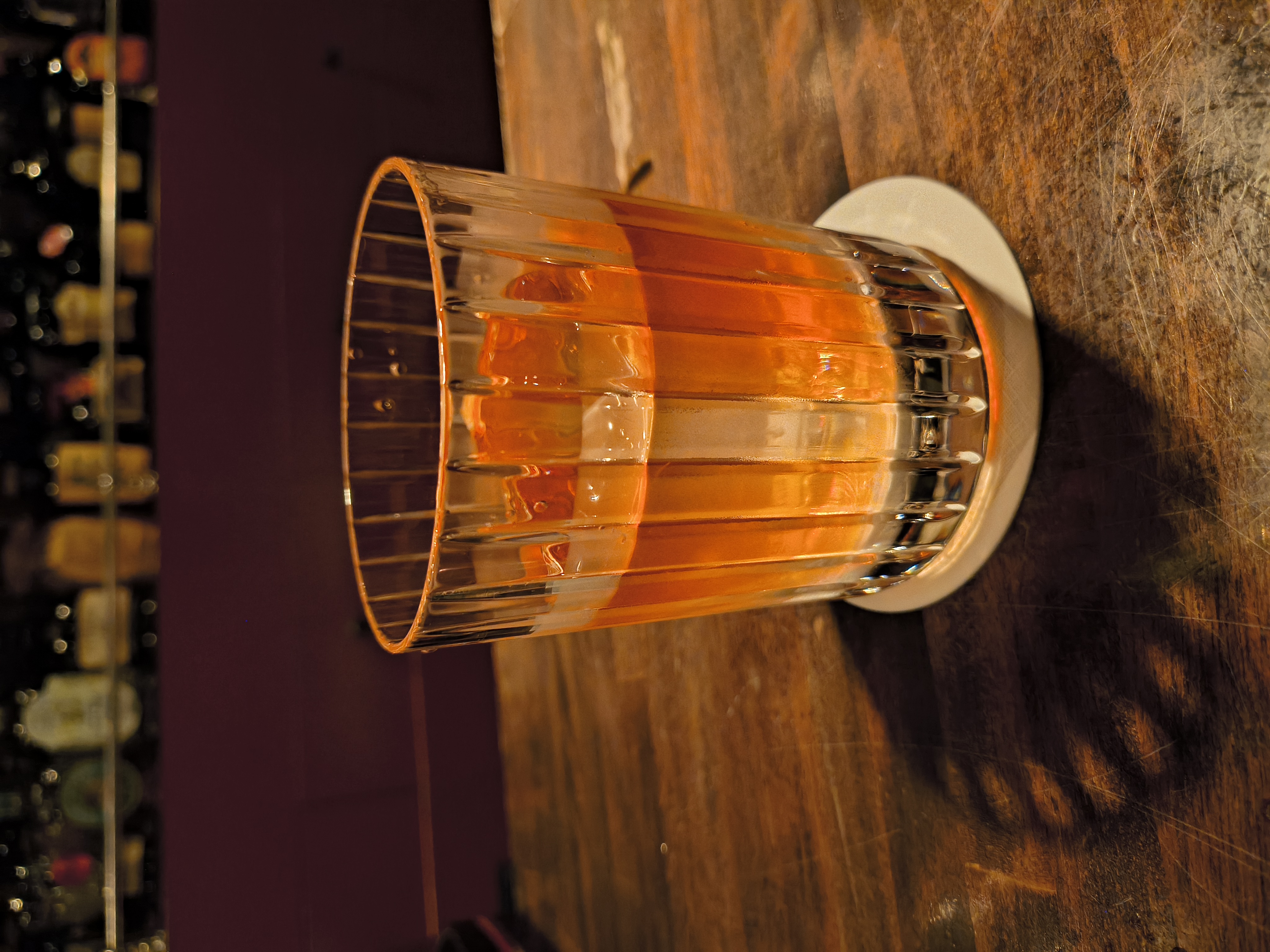 薄暗いバーで撮影。カクテルのグラスにピントが合い、背景のボトル棚はぼけている