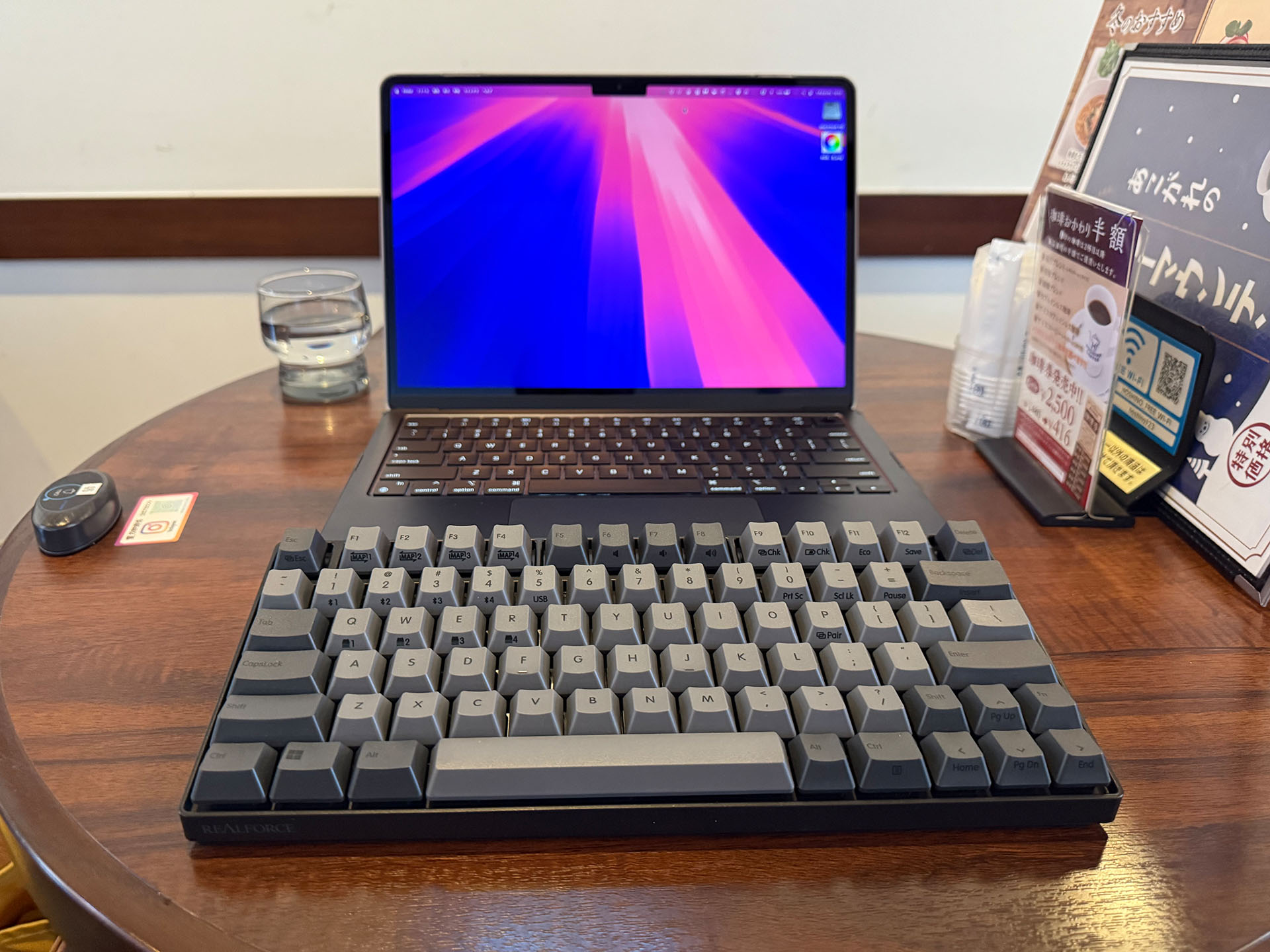 去年M3 MacBook Air 13インチとREALFORCE RC1でモバイルしたときの失敗を再現したもの。REALFORCE RC1をMacBookにどうにも乗せられなかったので、MacBookの手前にREALFORCE RC1を置いて使うカタチに。しかし実際は飲み物などを置くスペースがかなり狭くなり、それ以上にMacBookのトラックパッドが非常に使いにくく、仕事にならない。