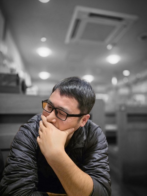 知人を酒場で撮影。新型カメラについて思案しているところをポートレートモードのカラーポイントで撮った。背景がモノトーンになり印象的な仕上がりだ