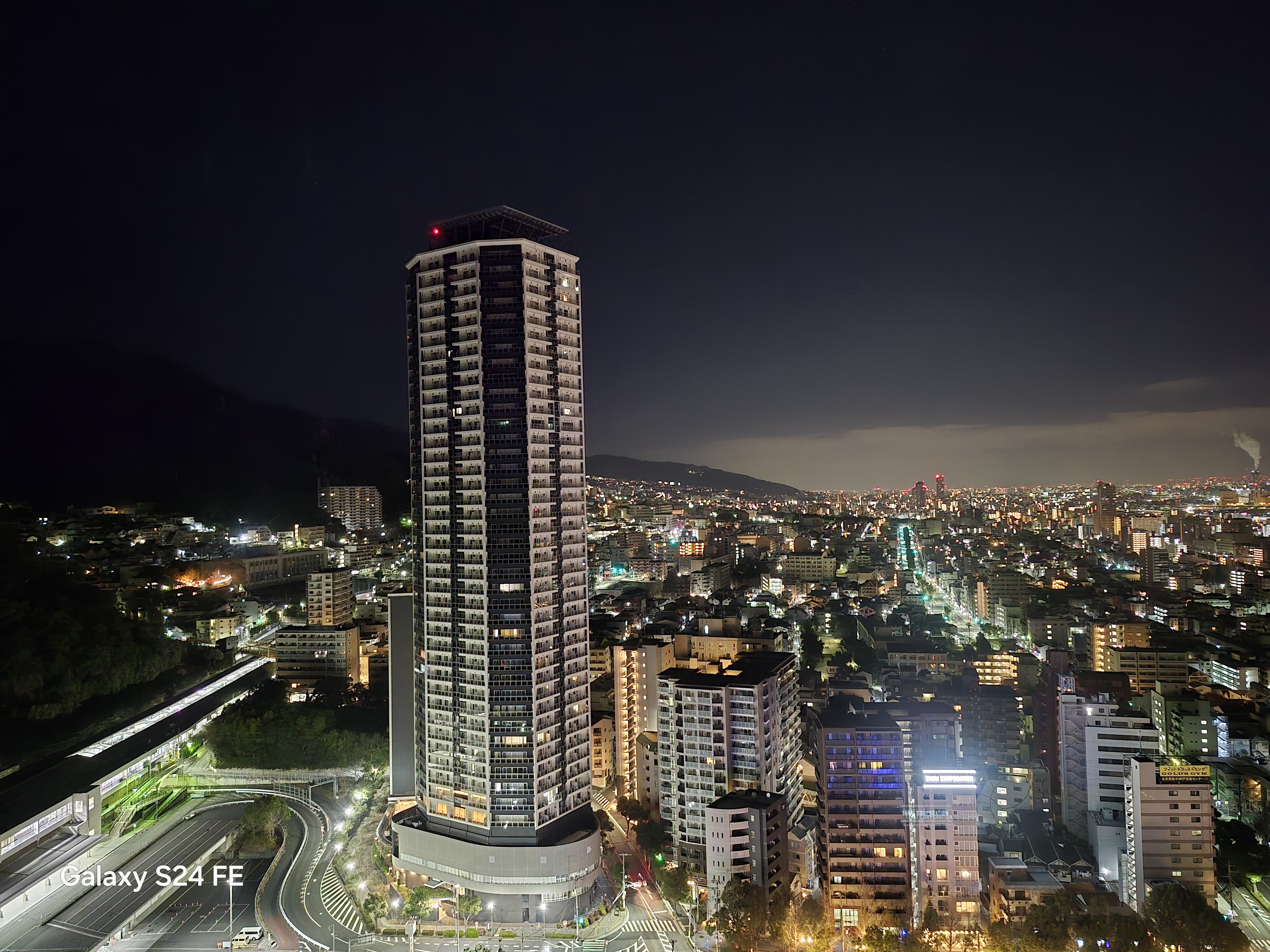広角カメラで夜景を窓越しに撮影。中央下の看板はやや白飛びしているが、近くの建物はくっきりと撮影されている