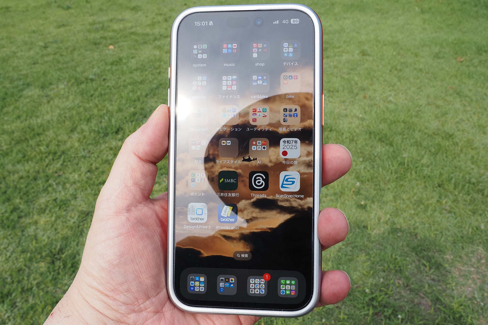 猛暑の炎天下でiPhoneを使っている様子。明るい空などが画面に映り込んで表示が見づらい。「あーもー見づらい！」というストレスにより、さらに汗が噴き出してイラつき増加！