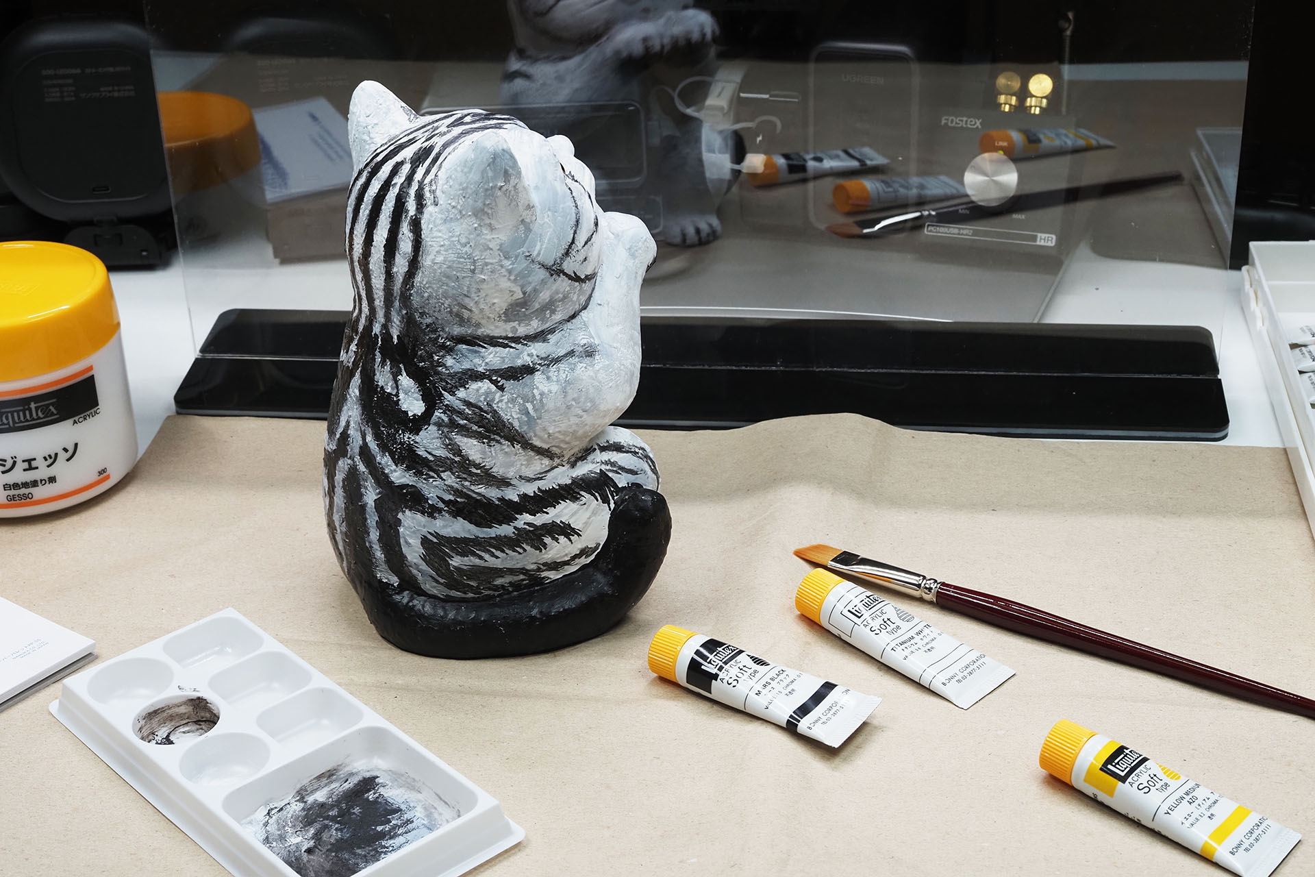 信楽焼の黒い猫の置物（タヌキっぽい）にジェッソを塗り、アメリカンショートヘアっぽい体毛を描いている。ジェッソをベッタベタ塗ったり、筆を速め強めに動かして体毛を描いたりしているが、ディスプレイ面への絵の具類の飛び散りは一切生じていない。