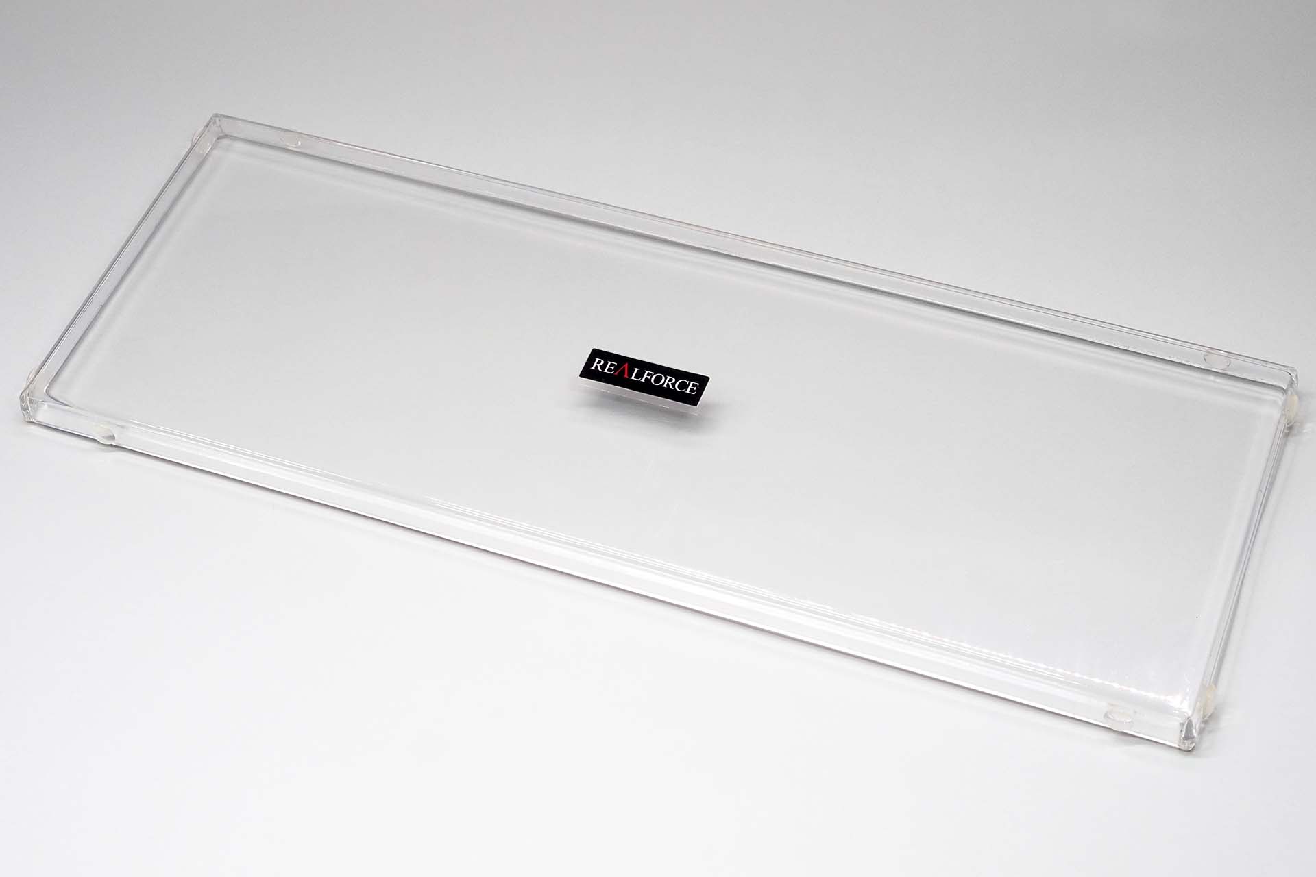 現在使用中のキーボードルーフ。透明ポリカーボネイト製で、キーボードのキー全体をカバーできるフタのようなものだ。確か……<a href="https://shop.bird-electron.co.jp/?pid=151785305" class="strong bn" target="_blank">バード電子「テンキーレス専用キーボードルーフ」</a>と同等のものだと思ったが……違うかもしれない。透明のゴム足は後から貼ったもの