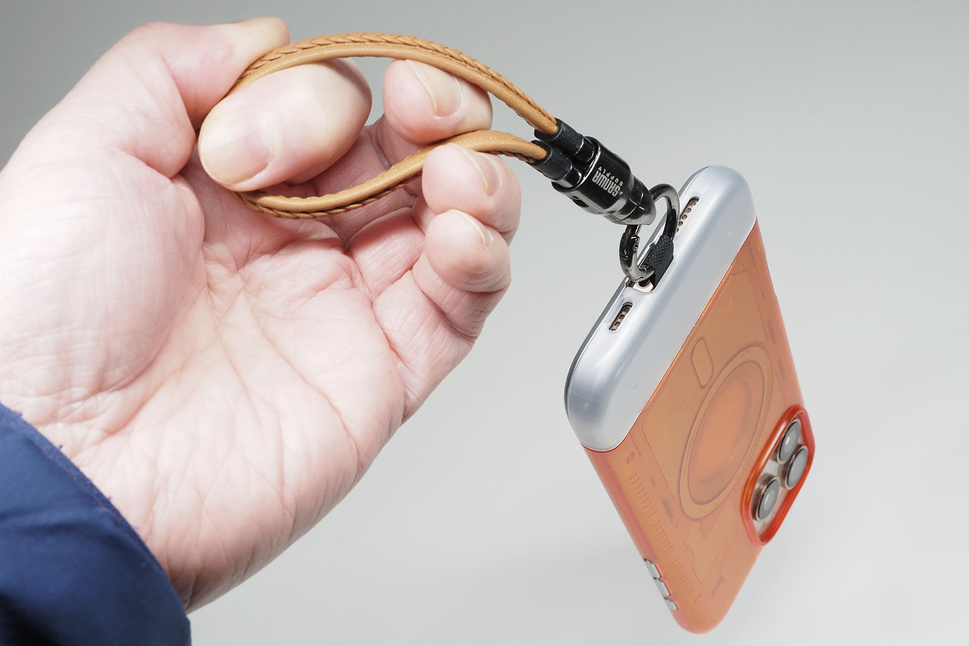 耐荷重5kgのストラップとして使える。ストラップ部分はポリウレタンレザーで、金具部分は亜鉛合金。スマートフォンとケースの間に入るT字のプレートは、ナイロン素材のような強靱っぽい樹脂プレート（柔軟／薄手）