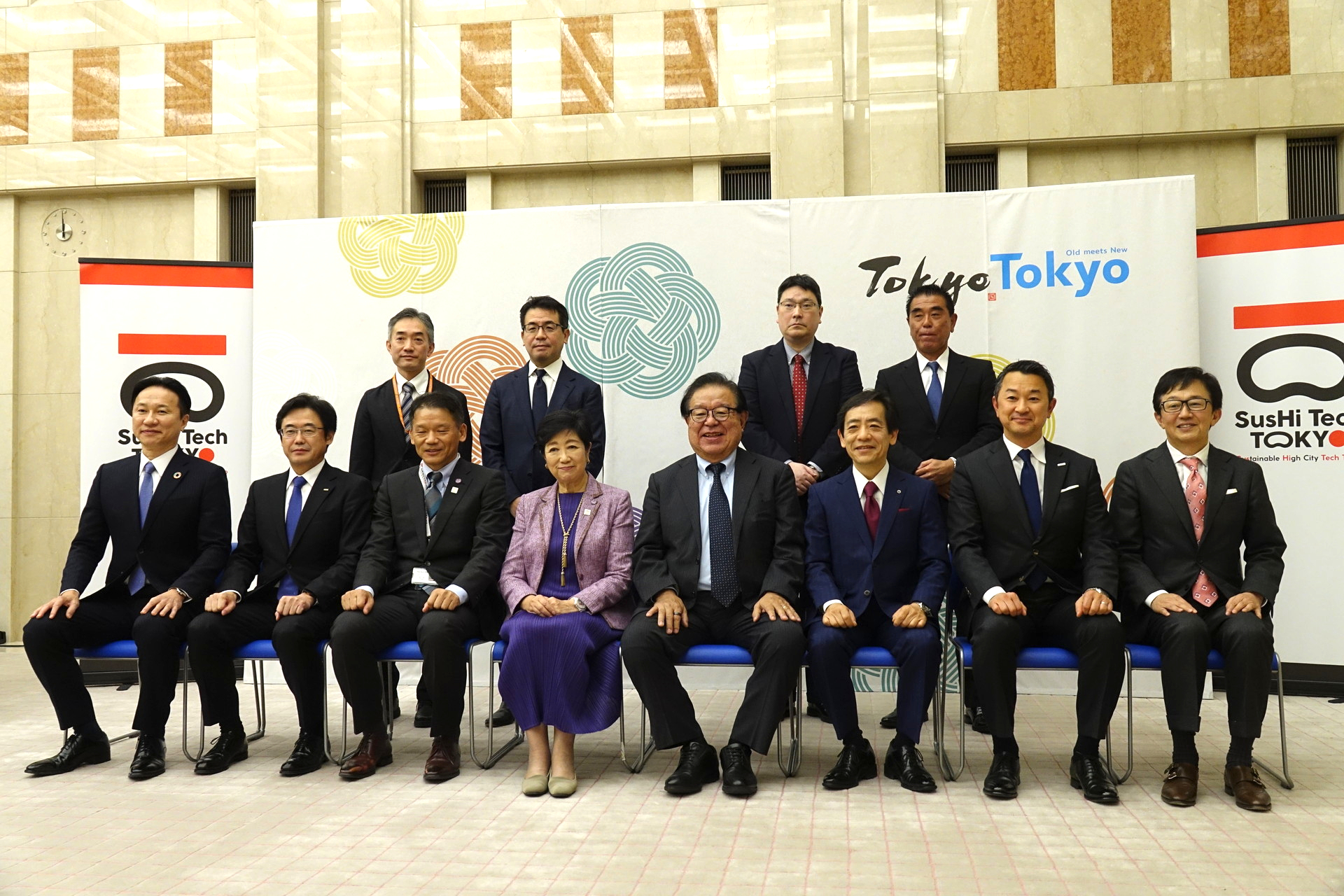 左後ろから時計回りに高野克己局長、JTOWER田中敦史社長、NTTブロードバンドプラットフォーム加藤成晴社長、ワイヤ・アンド・ワイヤレス向吉智樹社長、楽天モバイル鈴木和洋共同CEO、NTTドコモ前田義晃社長、NTT東日本澁谷直樹社長、慶応義塾大学村井純教授、小池百合子都知事、宮坂学副知事、KDDI松田浩路社長、ソフトバンク佃英幸専務執行役員兼CTO