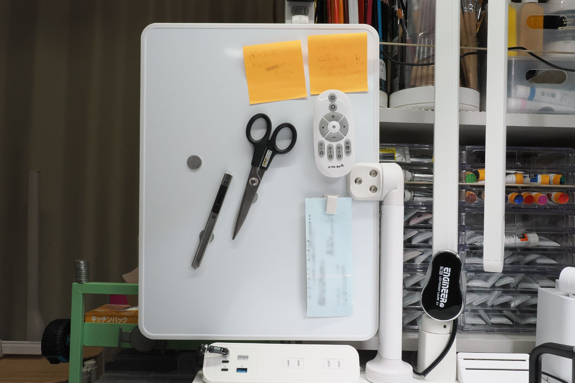 ホワイトボードに吸着させたネオジム磁石の上に、ハサミやカッターを吸着できる（カッターにはスチールプレートを貼っている）。つまりこういった「よく使うツール」の収納場所にもなる。