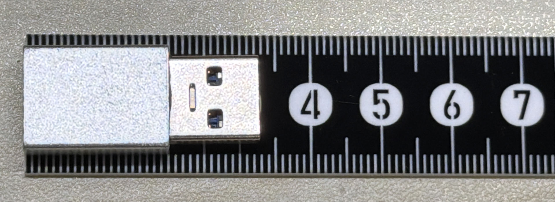 金属製のUSB変換アダプターを載せた状態。USB変換アダプターは反射で光っているが定規は反射していない。