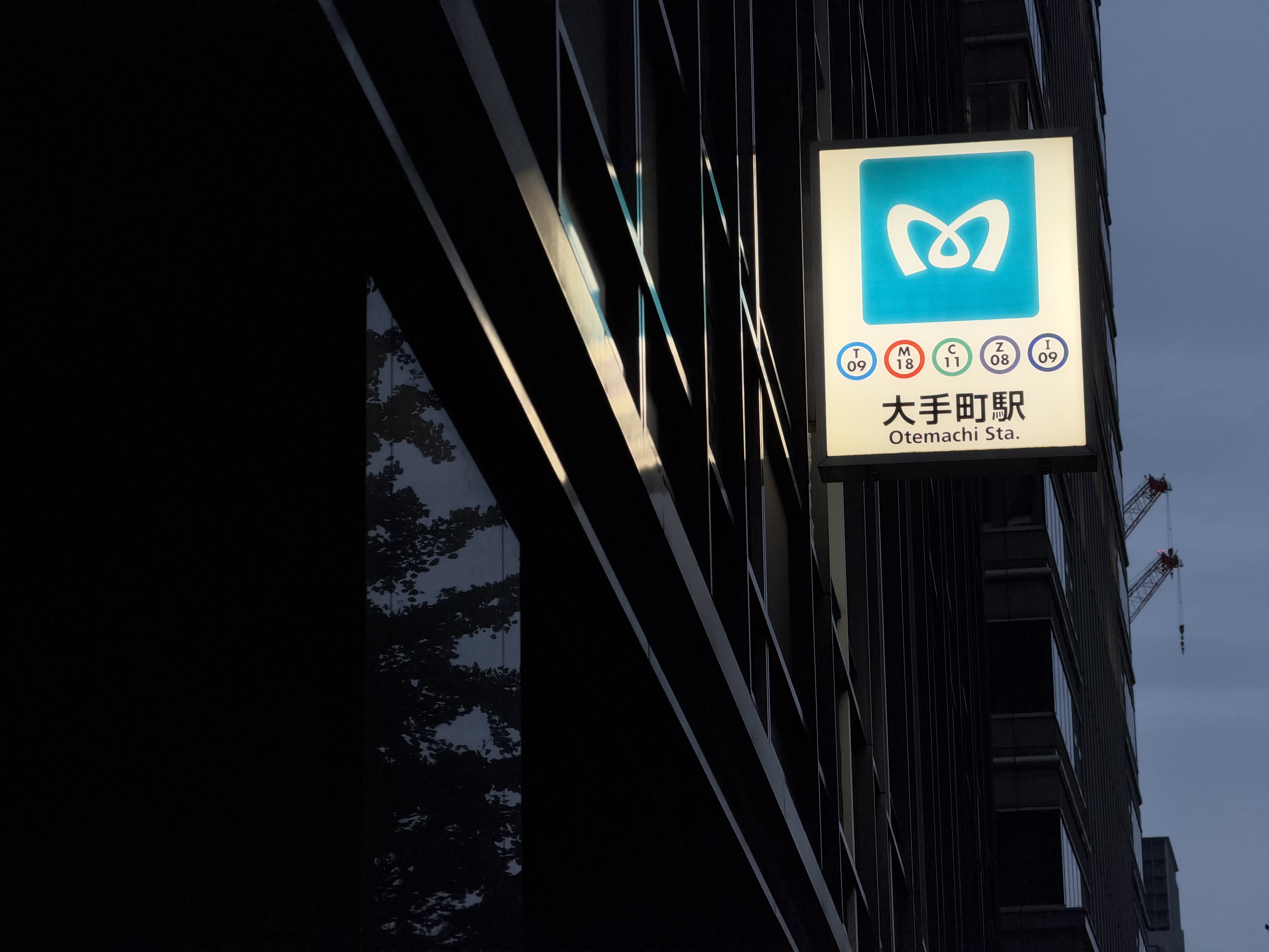 夕闇に沈むビル群を背景に、ぽつんと灯る地下鉄の看板を切り取った情景。暗部となる建物の黒く引き締まったシャドウの中で、看板の鮮やかな色彩と発光具合がひときわ目を引く仕上がりとなっている。