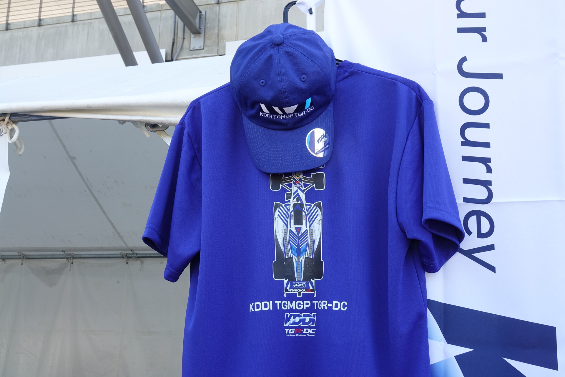 右はグッズTシャツを着用するチームドライバーの小林利徠斗選手の後ろ姿