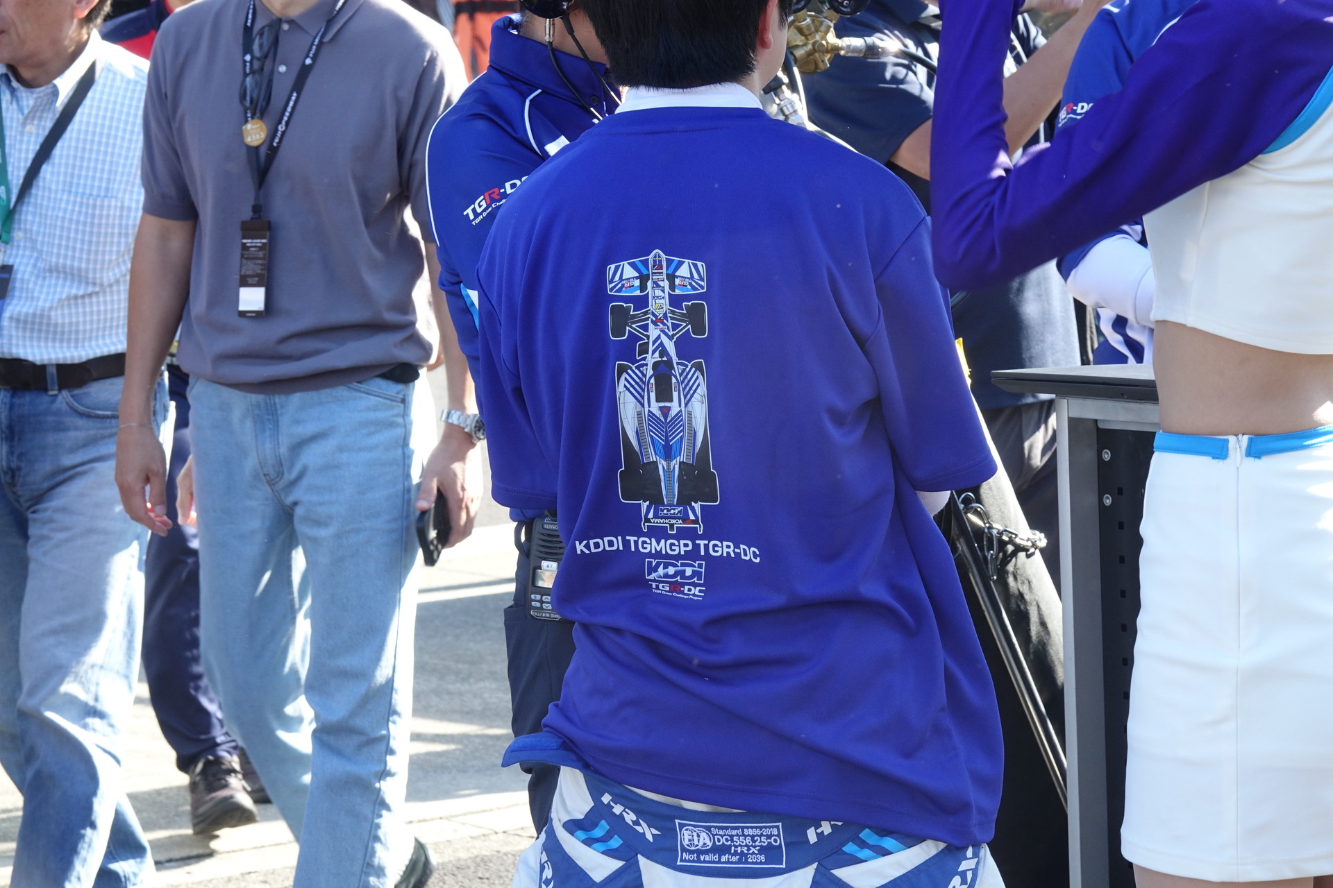 右はグッズTシャツを着用するチームドライバーの小林利徠斗選手の後ろ姿