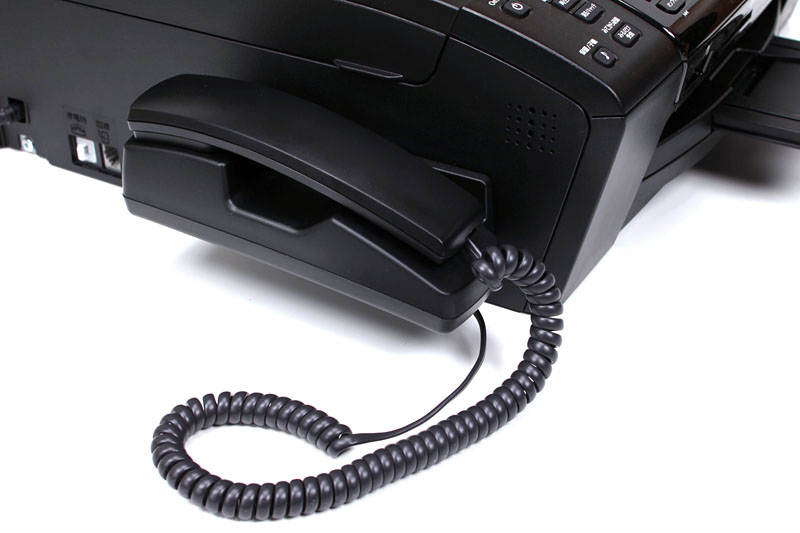 695CDNは電話/留守番電話機能付き。本体にはこのような受話器（付属）をセットでき、これとは別にワイヤレス子機（1台付属）を利用できる。留守番電話関連機能は695CDN本体の操作パネルから使用する