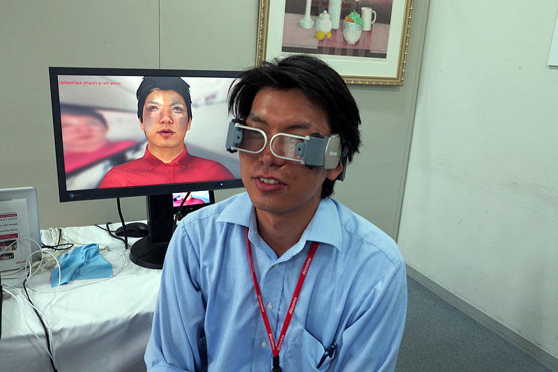 別の角度から見たところ。背後のディスプレイは、カメラで捉えたユーザーの姿をCGと実写（目付近は実写）で合成した姿