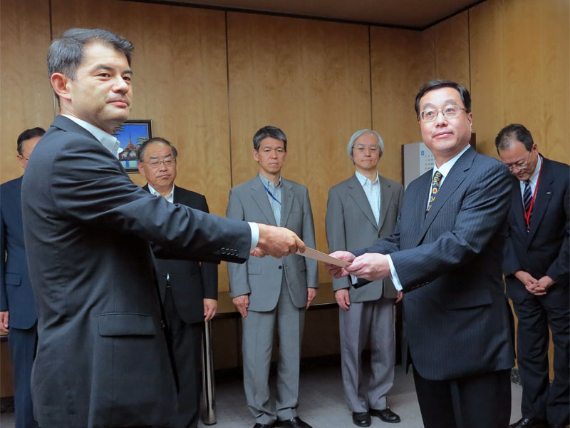 認定書を手渡す柴山副大臣（左）と受け取るUQ野坂社長（右）、野坂氏の後方に田中氏