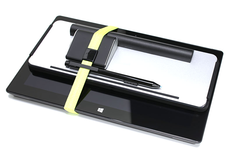 Wedge Mobile Keyboardを使ったら、Surface Proの画面の向きや顔からの距離を自由に調節できるようになった。写真に見えるマウスはマイクロソフトの「Wedge Touch Mouse」（http://k-tai.impress.co.jp/docs/column/stapa/20130624_604630.html#contents-section-3）。携帯時は、お弁当用箱類を束ねる伸縮ベルトでひとまとめにして持ち出そうと考えた。Wedge Mobile KeyboardのカバーとSurface Proの画面を向き合わせて束ねると、画面に傷が付くこともない