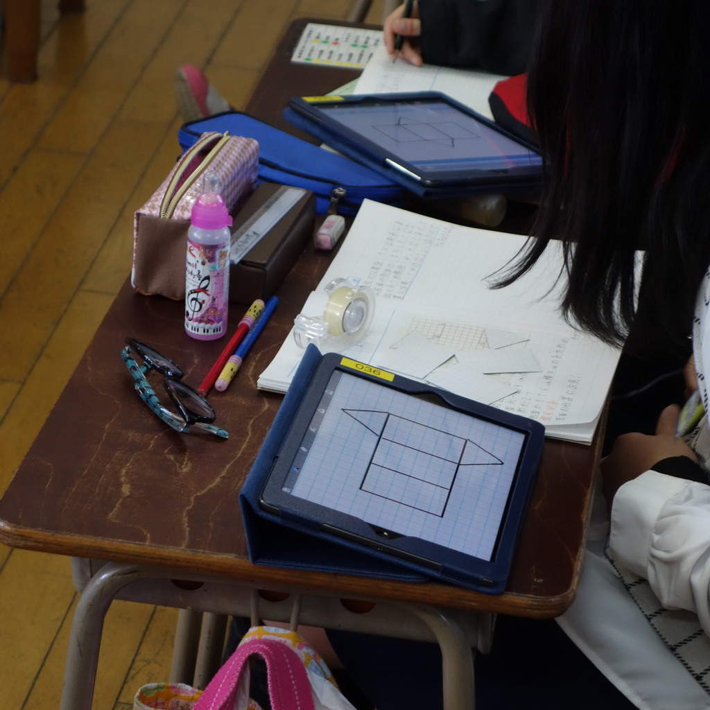 Tablet Syncというアプリを使い、iPadに表示された方眼紙に三角柱の展開図を書いている。紙や糊、鉛筆といった道具も併用されている