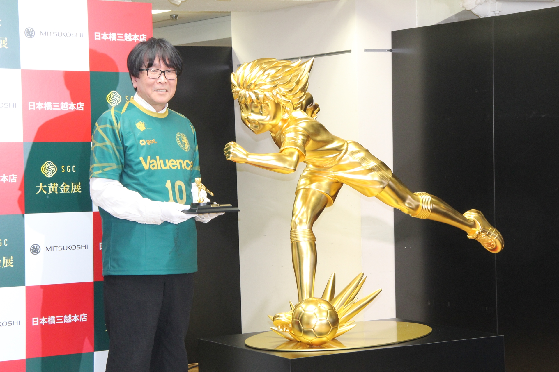 「金箔CAPTAIN TSUBASA」の隣で純金のキャプテン翼像を持ち、ツーショット（？）撮影に臨んだ高橋氏
