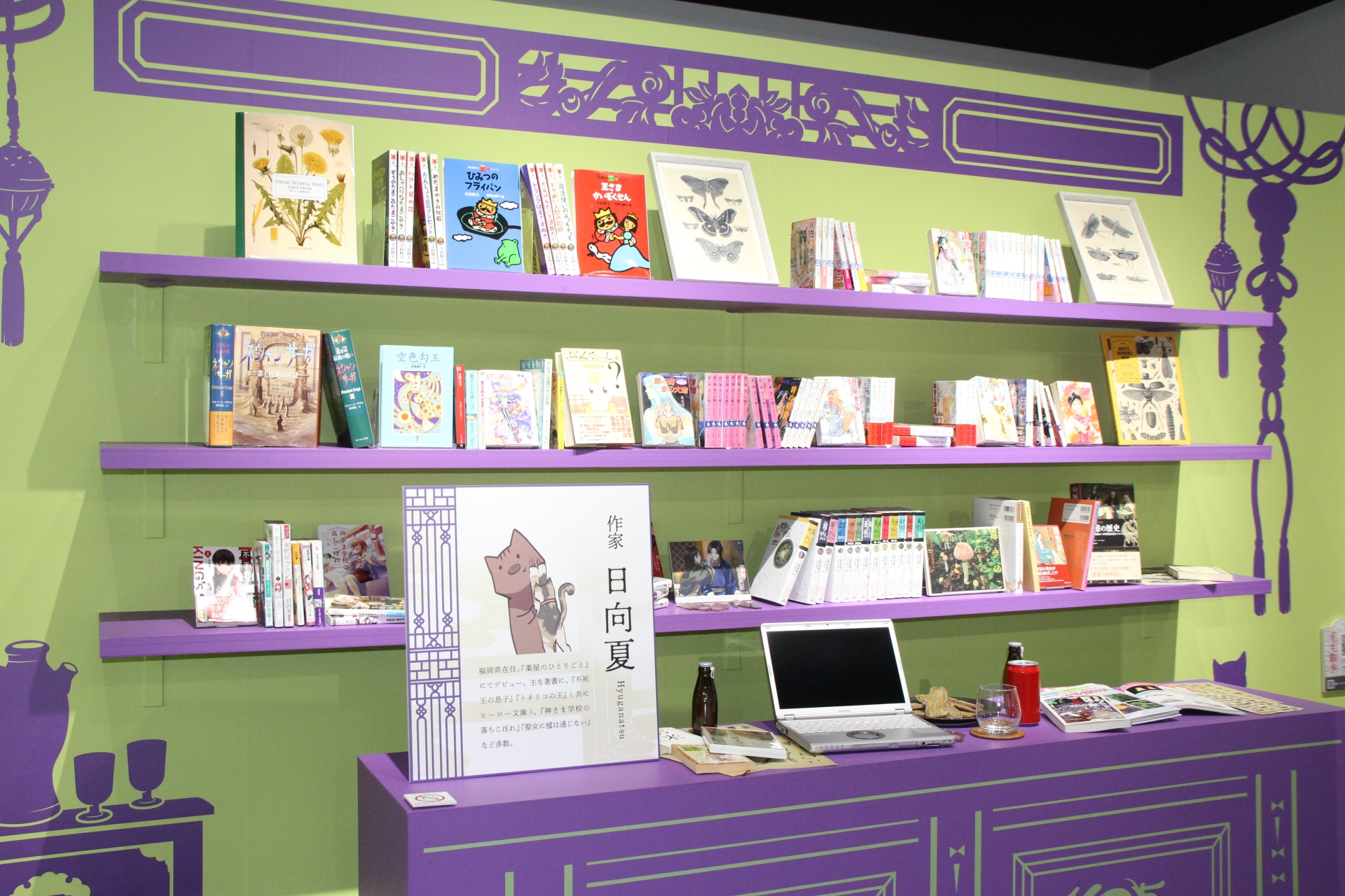 “作家 日向夏をひもとく”と題したコーナーでは、日向夏氏の机周りをイメージ的に再現してあるほか、日向夏氏のひとりごとというスペースでは、日向夏氏がX（旧Twitter）でつぶやいた“ひとりごと”が吹き出し形式で掲載されているのを読むことができる。左下の“毛毛（マオマオ）散歩”は、ここにスマートフォンのQRコードリーダをかざすと、毛毛のアニメーションを見ることができる。4カ所は会場内にあるが、5つ目は会場から徒歩4分のところにあるLATTEST ミズマチにて開催されている<a href="https://iimono-mart.jp/kusuriya-cafe/" class="n" target="_blank">コラボカフェ</a>の中に掲示されている