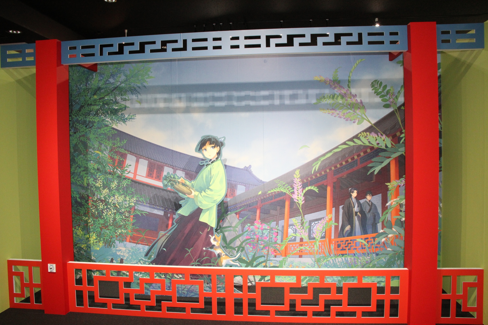 “イラストレータ しのとうこ画回廊”の途中には、フォトスポットとして野草を摘む猫猫と、通路を歩く壬氏、その従者高順（ガオシュン）をバックに撮影できる場所が用意されている