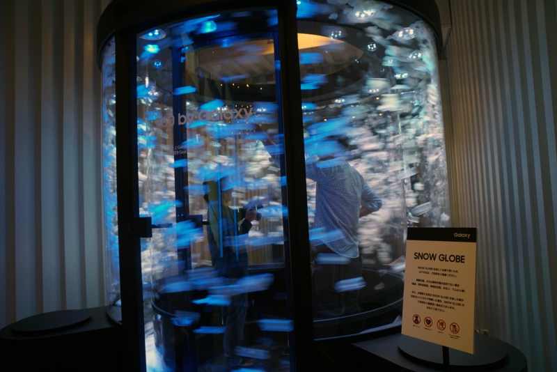 ガラスで囲まれた円形空間に入り、内部で吹き荒れる花びらを360度カメラの「Gear 360」で撮影して楽しむアトラクション「SNOW GLOBE」。Gear 360は4K解像度に対応したカメラで、手軽に持ち運べる携帯性やライブビュー撮影機能、IP5X/IPX3の防塵・防滴仕様などを特徴としている