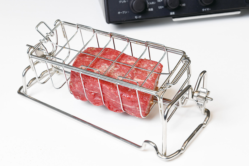 肉をかごにセットする<BR>付属のロティかごに肉を入れて、ふたを閉じ、フックを止める。ふたは肉の厚みが4.5cm以上なら膨らみを上に、4.5cm未満なら膨らみを下にしてセット。肉の厚み6.5cmまで対応できる