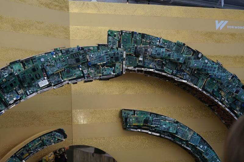 最近米国のイベントでよく見かける自撮りマシンのコーナー。写真を撮影してその場で、印刷して来場者に渡すシステム。そのアーチは、過去の基板から構成されていた。チップやボードの型番などは消されていたのだが、なぜか競合他社のロゴは消されていなかった……