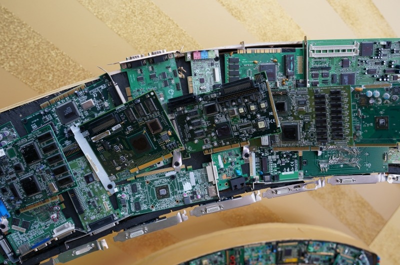 最近米国のイベントでよく見かける自撮りマシンのコーナー。写真を撮影してその場で、印刷して来場者に渡すシステム。そのアーチは、過去の基板から構成されていた。チップやボードの型番などは消されていたのだが、なぜか競合他社のロゴは消されていなかった……