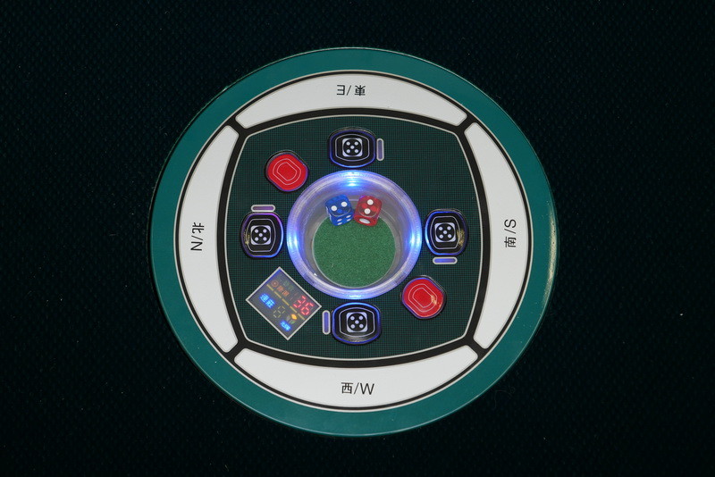 これが中央のパネル。日本の全自動麻雀卓とは異なって円形で、中央にサイコロが2個あり、横のサイコロボタンを押すとサイコロの底面が回ってサイコロが振られる。赤いボタンは牌を入れ替えるときに押すボタンだ