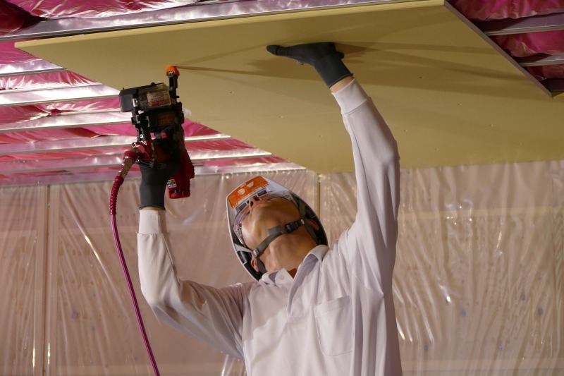 脚立の上で重量物を片手で支えながらビスを打つ