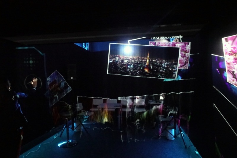 奥に座席があり、その前に画面が表示されている。画面上の写真は手で払ってどけると言ったことも可能