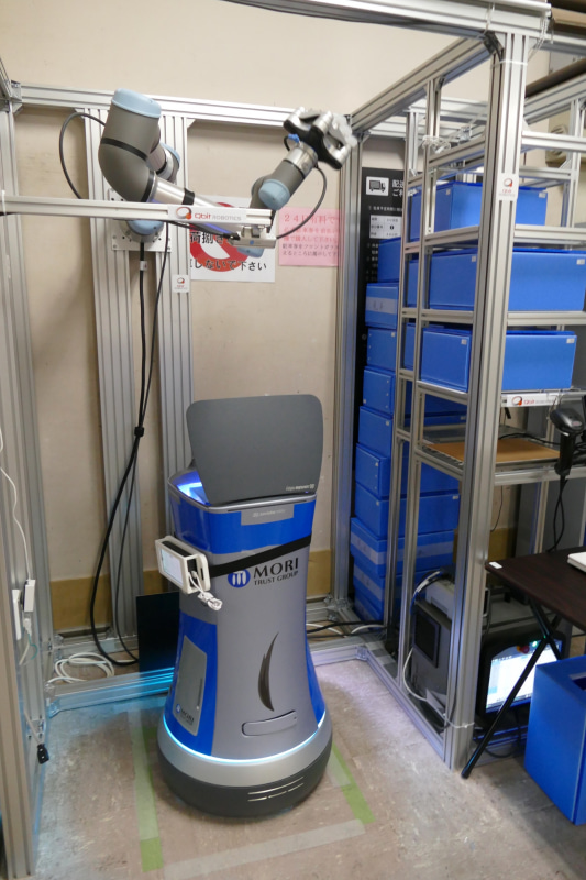 運搬ロボットと連携する「ロボットアーム搭載荷物棚」