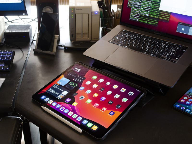 仕事場のiPad Pro 12.9+Smart Folio+Apple Pencil(第2世代)。メインテーブルの右にあるコーナーテーブルに配置したのでなにかの時にすぐ手書きできる。Apple Pencil(第2世代)は側面に磁石で付き、ペアリングと充電が容易。上側にMacBook Pro 16、左上小さいボックスが第10世代NUC。メインディスプレイがBenQ SW240+フード。M1 Mac miniは写真外の左端にある