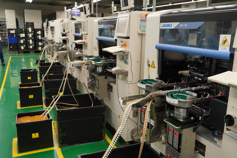 DIP工程。足のあるチップやコンデンサなどは自動で、スロットのように大きなものは人の手で載せていき、最後にハンダ付けを行なう