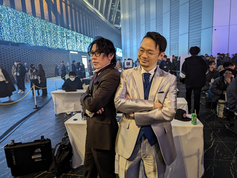 1巡終わる毎に休憩時間が設けられており、その間は観戦に来ていた他チームの選手らと談笑したり、挨拶を交わすシーンを見かけるなど、プロ格闘ゲーマーたちとの距離感の近さが感じられるイベントとなっている。写真はファンと交流している実況のアール氏、解説のハメコ。氏