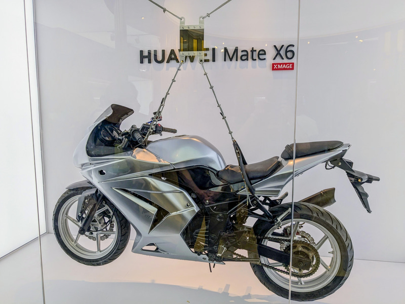 HUAWEI Mate X6の本体内部にあるカーボンファイバーの耐久性を示すデモ。バイクを吊るしても大丈夫