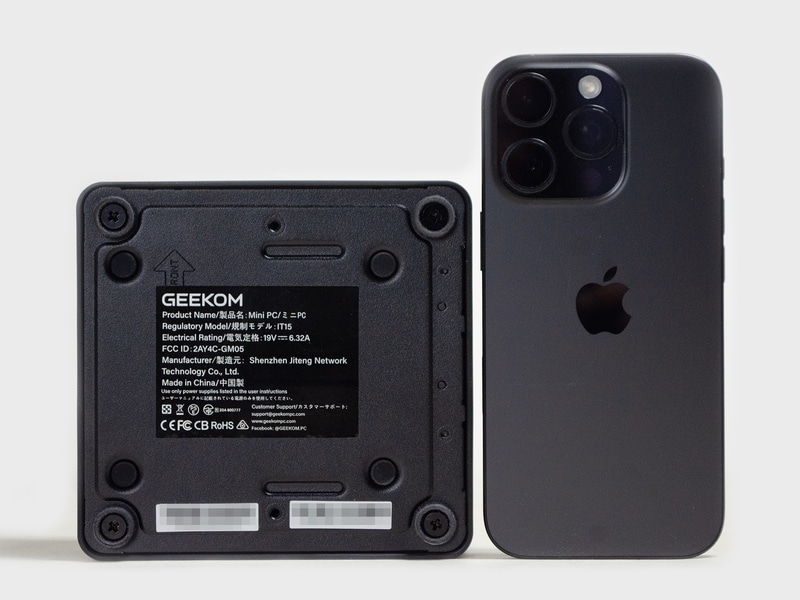 裏面とiPhone 16 Pro。四隅にゴム足とその中央にネジ。内側にVESAマウンタ用ネジ穴。サイズはミニPCとしては一般的