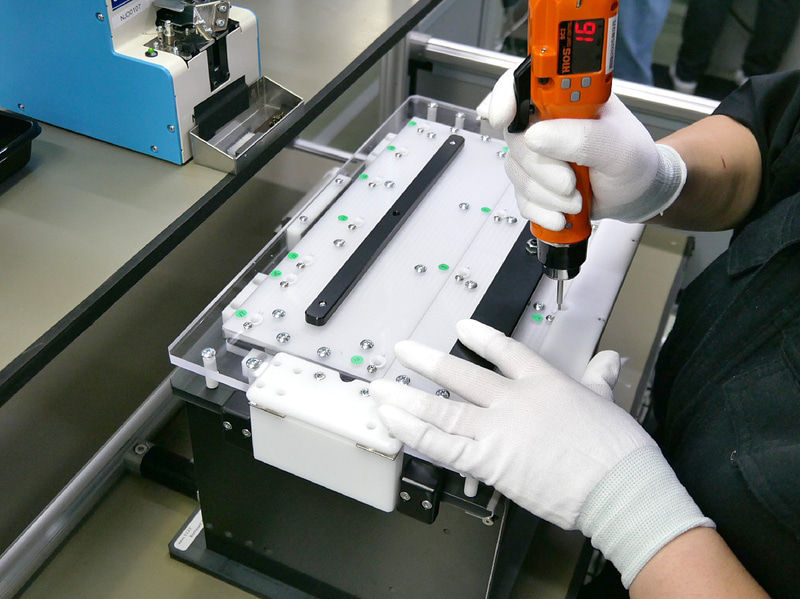 ボトムケースのネジ締め作業。治具を使って正しくネジ締めを行なう。この治具も新品の生産ラインで使用しているものだ