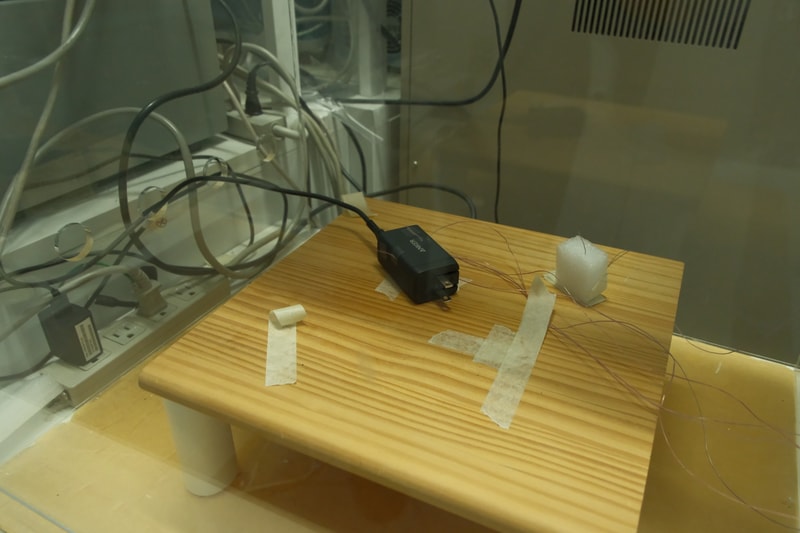 ACアダプタのテスト装置。周囲の風に影響されないよう、ケースの中で温度を測定している