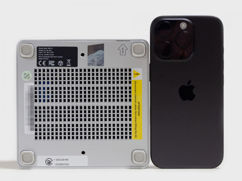 裏面とiPhone 16 Proの比較。四隅にゴム足、VESAマウンタ用のネジ穴 x2。ミニPCとしては標準的なサイズ