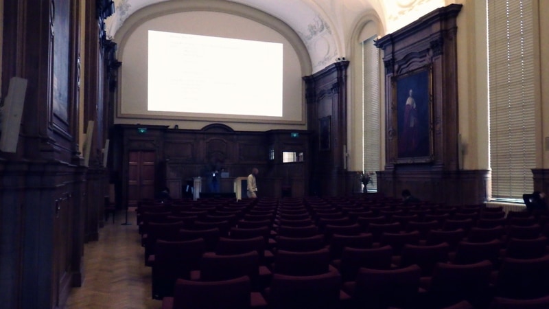 IMW 2026の会場となった「University Hall(大学ホール)」。アーチ形の天井がかなり高い。正面の上部に投影スクリーン、下部に演台がある。左右の壁には肖像画が飾ってあり、内装と相まって伝統を感じる。2026年5月10日(現地時間)に筆者が撮影したもの