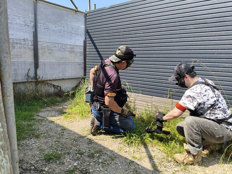 ダウン後の誤射を避けるため、日向側で衛生兵による救援を待っている筆者。建物内は風が遮られるため、さらに暑く感じられた