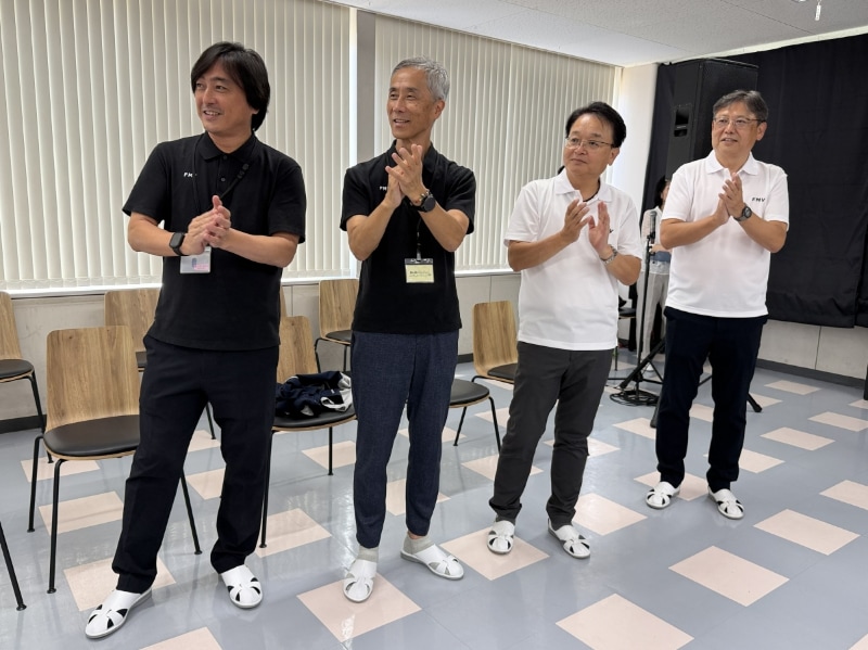 入場する参加者を拍手で迎え入れる(左から)富士通クライアントコンピューティング 執行役員常務/COOの栗田克彦氏、富士通クライアントコンピューティング執行役員常務/コンシューマ事業本部長の髙嶋敏久氏、島根富士通の執行役員副社長の山根淳氏、島根富士通の宮下浩之社長