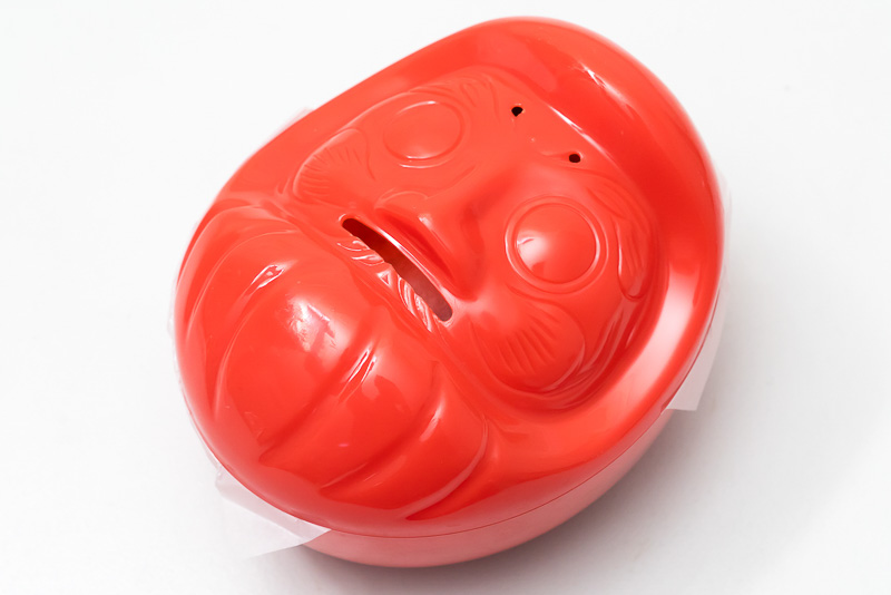 だるま弁当の容器。ダルマを模していて、食べた後は開いている口から硬貨を入れ、貯金箱にもなりそう