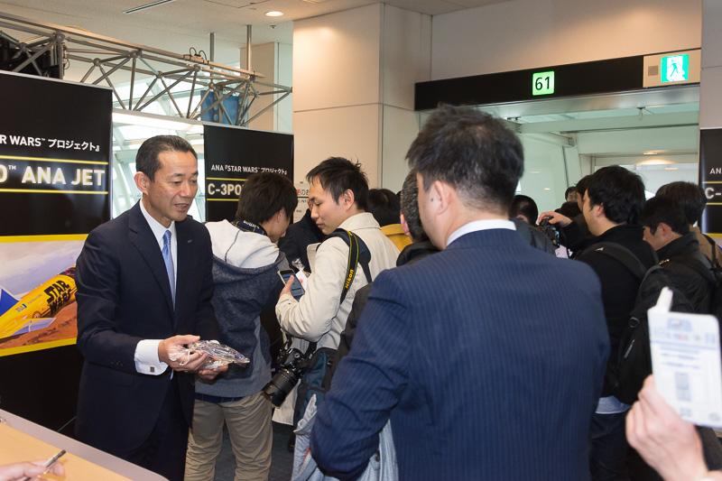 ANA東京空港支店長の峯尾氏やアンソニー・ダニエルズ氏らが、搭乗口で初便搭乗記念品を配布