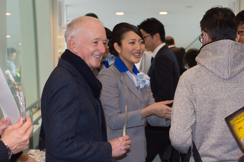 ANA東京空港支店長の峯尾氏やアンソニー・ダニエルズ氏らが、搭乗口で初便搭乗記念品を配布