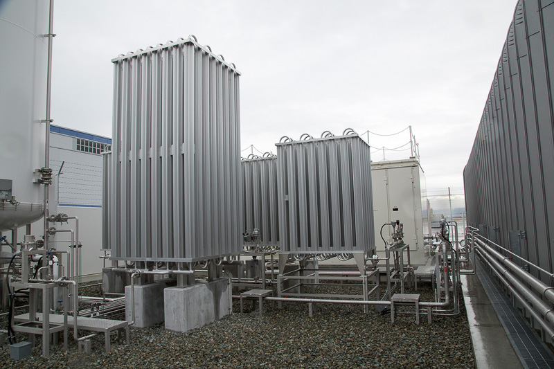 銀色で冷却フィンが付いているのが熱交換により液体水素をガス化させる蒸発器。そのあと、圧縮機で40MPaまで昇圧させる。蒸発器の下のみ砂利が敷き詰められているが、これは液体水素が蒸発する際に周辺の空気や窒素が凍ることがあり、それが下に落ちると一気に蒸発するなどの危険があるので砂利を敷いているという説明だった