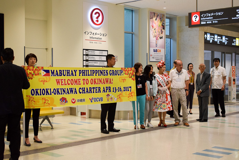 横断幕でお出迎え。セレモニー参加者は拍手で来沖客を迎えた