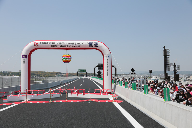 テープカットは、木津川橋の中央付近で行なわれた。写真向かって右の上り車線には、城陽市主催の「開通直前フリーウォーキング」参加者たちが集まっている