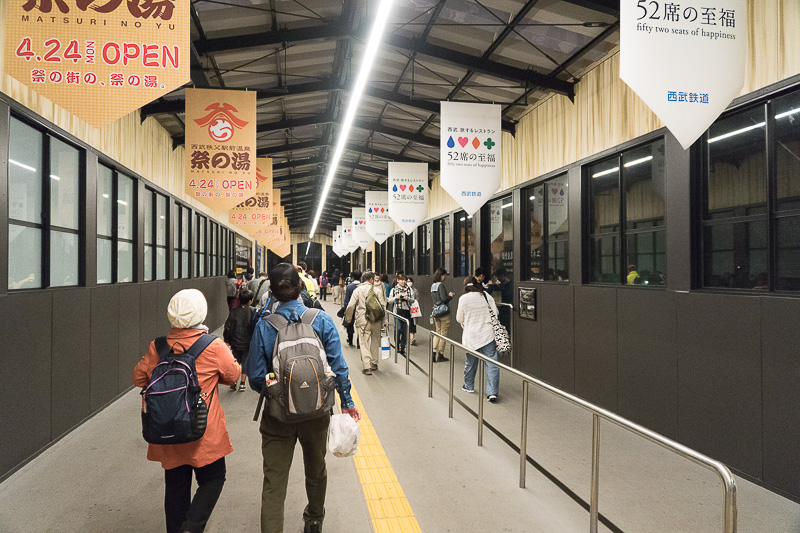 保線橋上を進む。4月に西武秩父駅前にオープンした「祭の湯」とレストラン列車「52席の至福」の広告