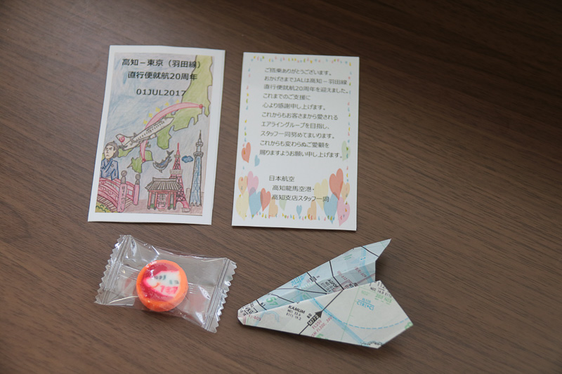 磯村康志支店長や歴代の制服を着用したJALスタッフらが、乗客に記念品を手渡していた。記念品はメッセージカード、アメ、航路図で折った紙飛行機