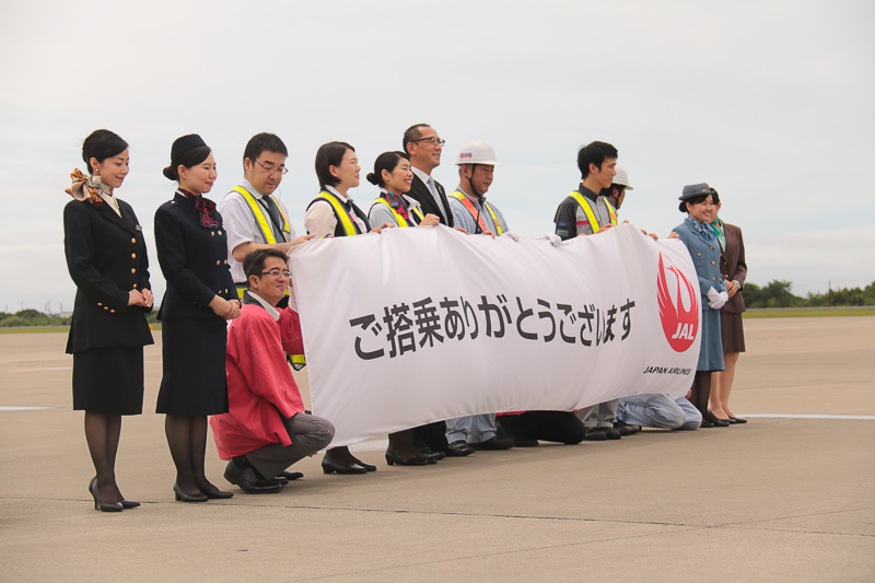 「ご搭乗ありがとうございます」の横断幕を持ってお見送りをするJALスタッフ